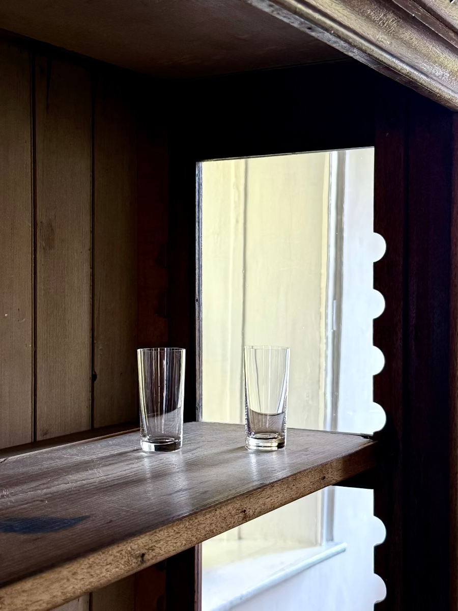 Two Deborah Ehrlich Simple Crystal shot glasses in a wood vitrine in front of a deep window