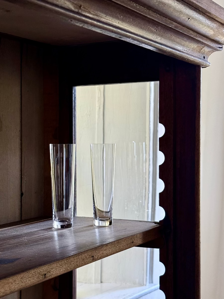 two straight stemless crystal champagne in a dark wood vitrine in front of a deep window