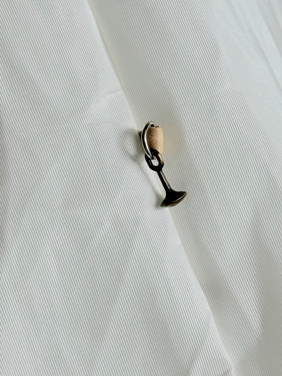 A small cast brass pull dangling from a silver d-ring attached to a travel bag with a tan piece of leather strap.