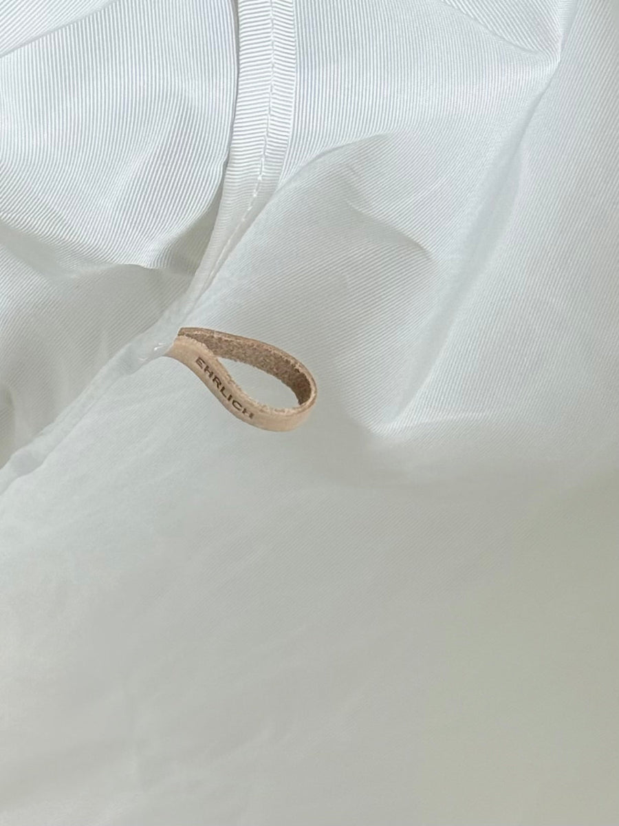 A close-up of the interior of a white sailcloth travel bag with a small beige leather loop tag attached, featuring the brand name 'EHRLICH' printed on it.