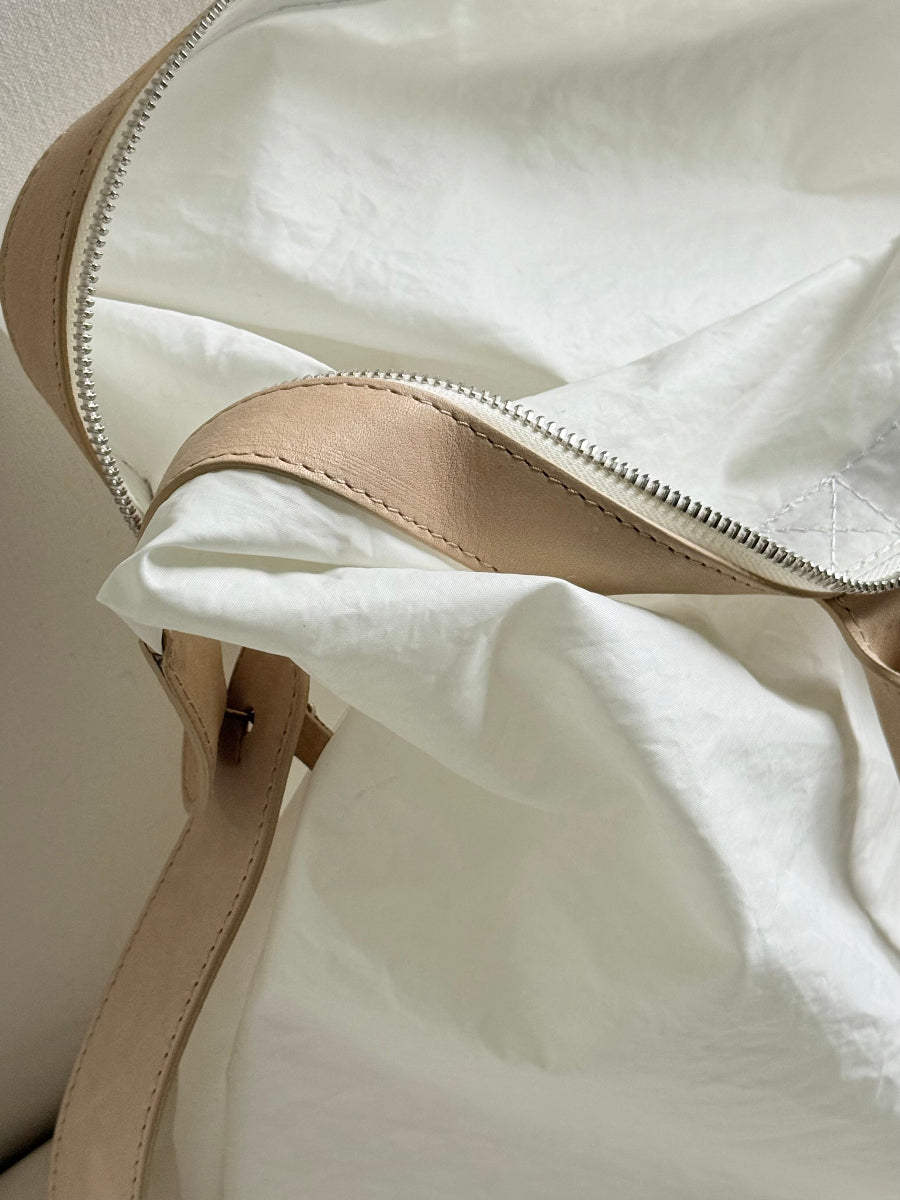Close-up of a beige leather strap and zipper trim on a white sailcloth travel bag, showing the texture and details of the interior construction.