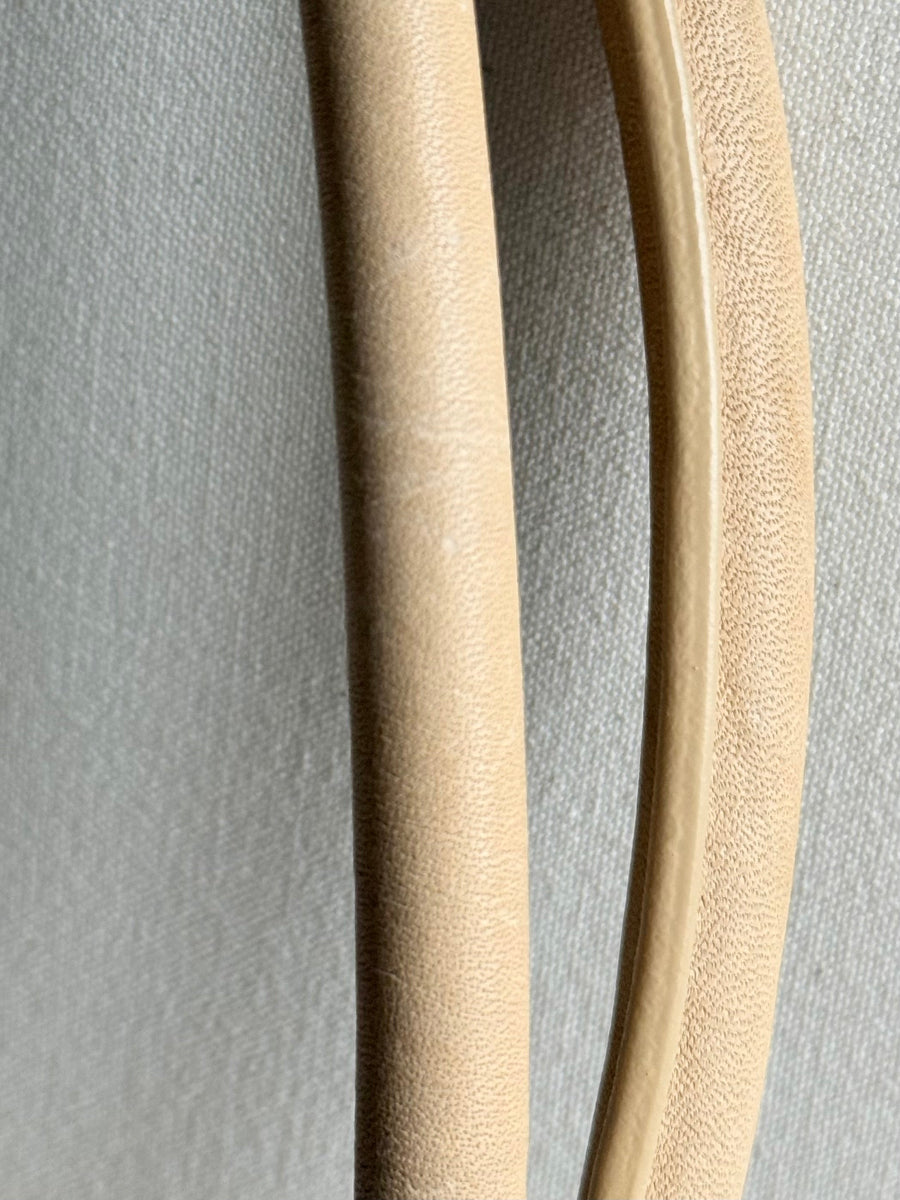 Close-up of two curved, textured beige leather straps, displayed against a neutral gray textured background.