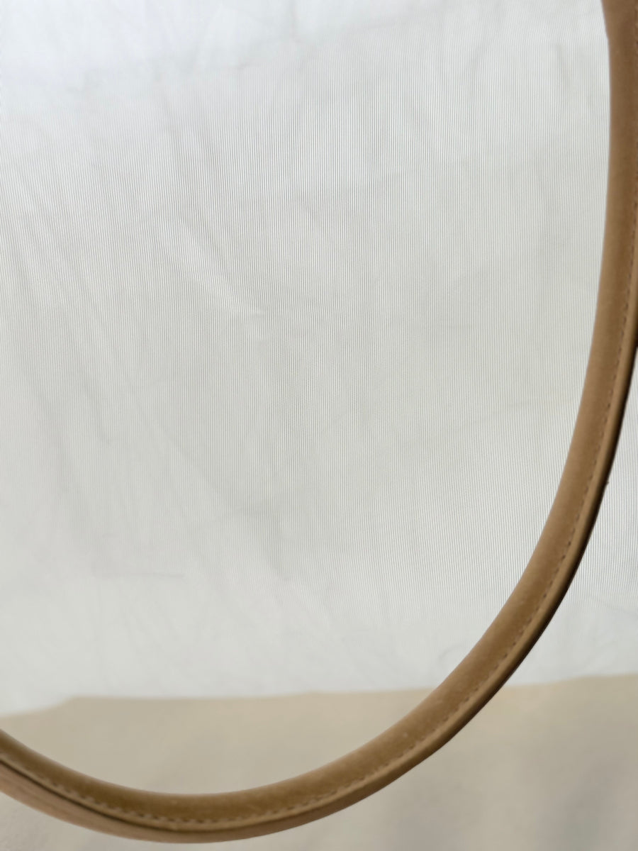 Close-up detail of a light tan leather strap against a white sailcloth travel bag.
