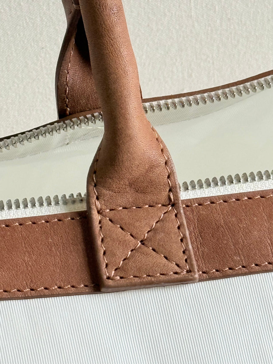 Close-up detail of a brown leather bag handle attached to a cream-colored zipper with visible silver zipper teeth.