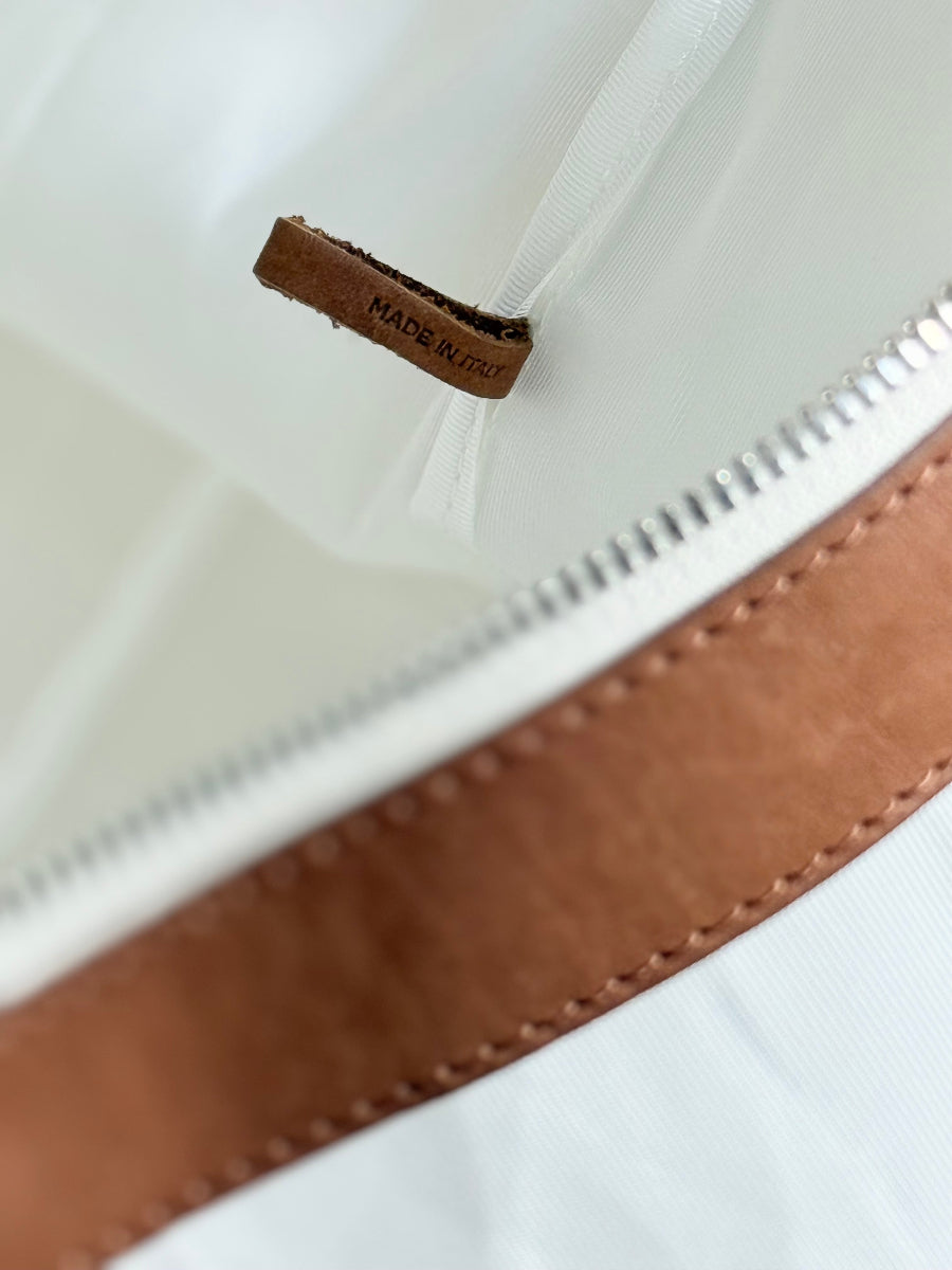 Close-up of a white interior of a travel bag with a brown leather trim and a small brown leather tag that reads 'MADE IN ITALY'.